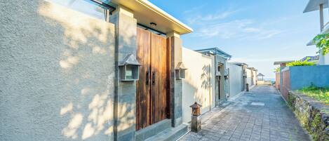 A narrow paved pathway leading to a building with a wooden door and a small lantern.