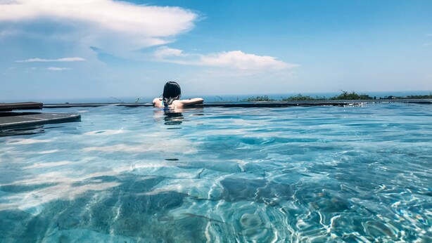 Une piscine aux eaux cristallines où une personne nage, le tout baigné d’un ciel dégagé et entouré d’un paysage lointain.