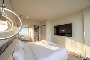 Ein modernes Hotelzimmer mit einem großen Bett, einem an der Wand befestigten Fernseher und einem durch eine geöffnete Tür einsehbaren Badezimmer.