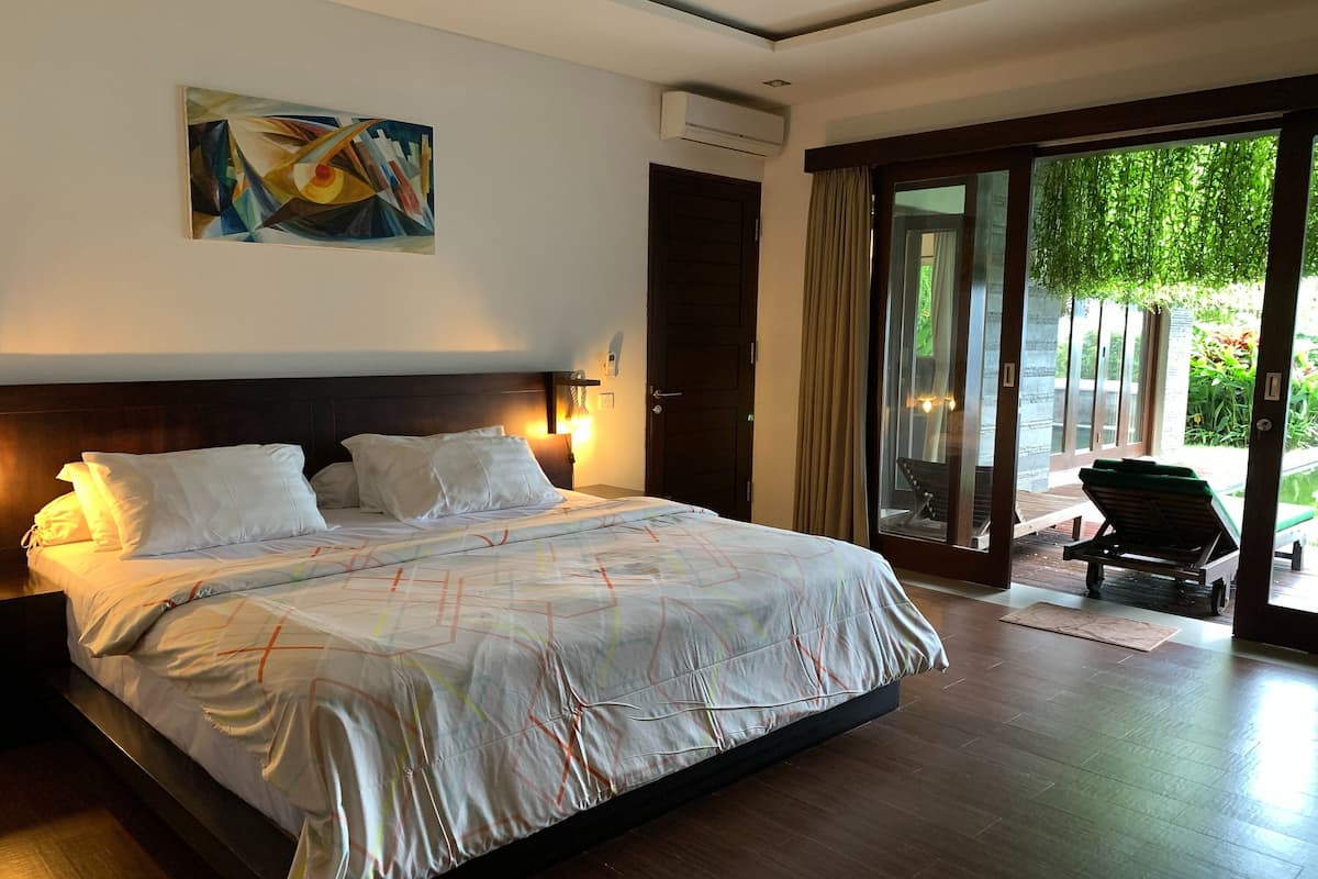 Ein Hotelzimmer mit einem großen Bett, einem Gemälde an der Wand und einer Glasschiebetür, die zu einem Außenbereich führt.