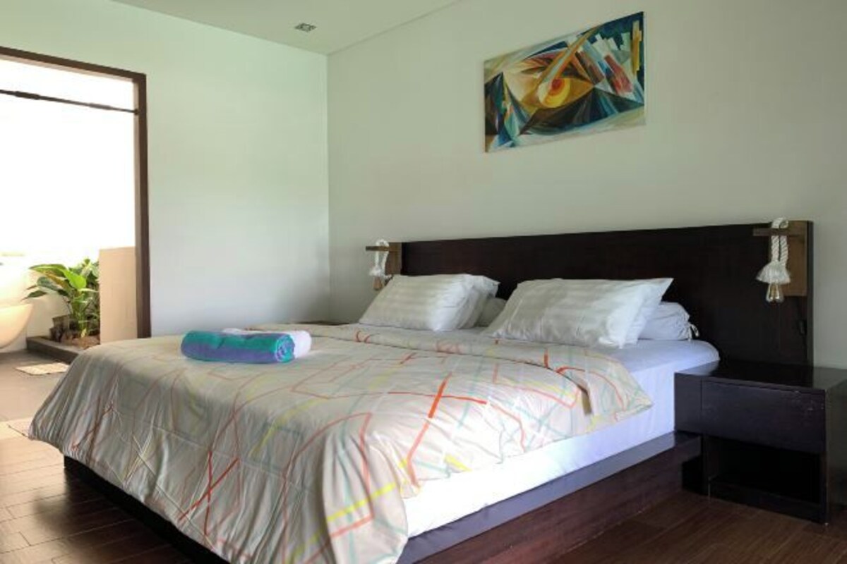 Een moderne slaapkamer met een groot bed, een nachtkastje en een schilderij aan de muur.