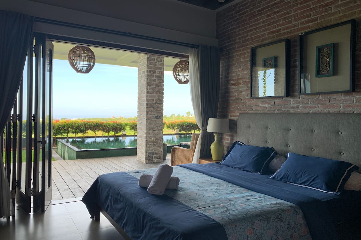 Ein Schlafzimmer mit einem großen Bett, Blick auf einen Pool und einer Ziegelwand.