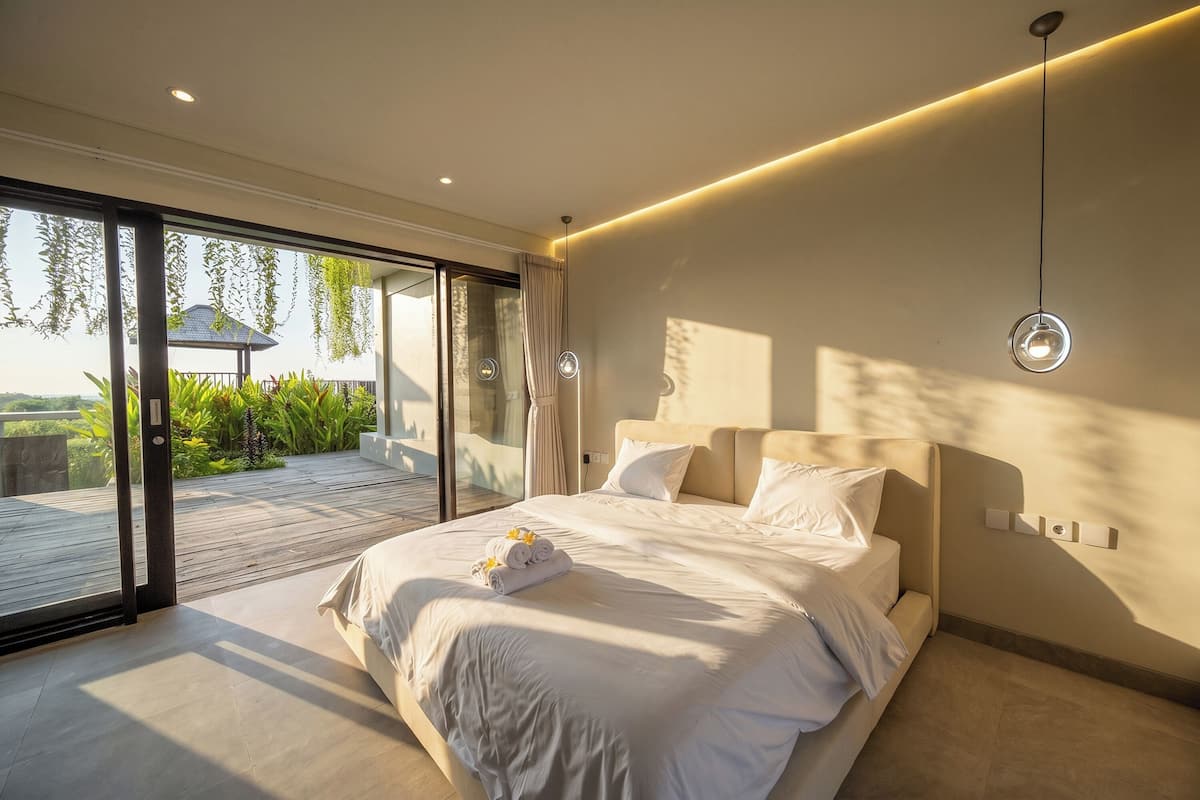 Ein modernes Schlafzimmer mit einem großen Bett, einer Glastür zu einem Außenbereich und einer Deckenleuchte.