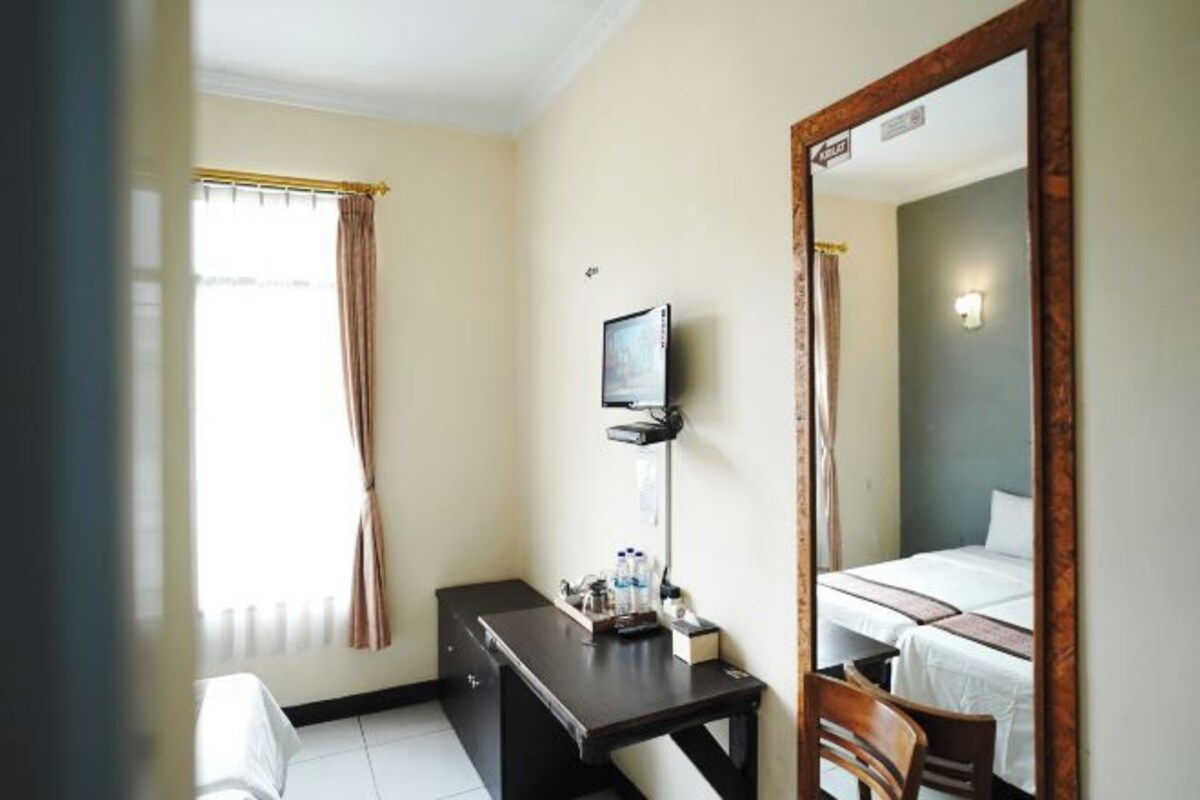 A hotel room with a bed, a desk with a chair, a television mounted on the wall, and a window with curtains.