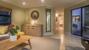 A spacious living room with a wooden coffee table, a sofa, and a large window with blinds. - Atlantic Bay Lodge (Cape Town)