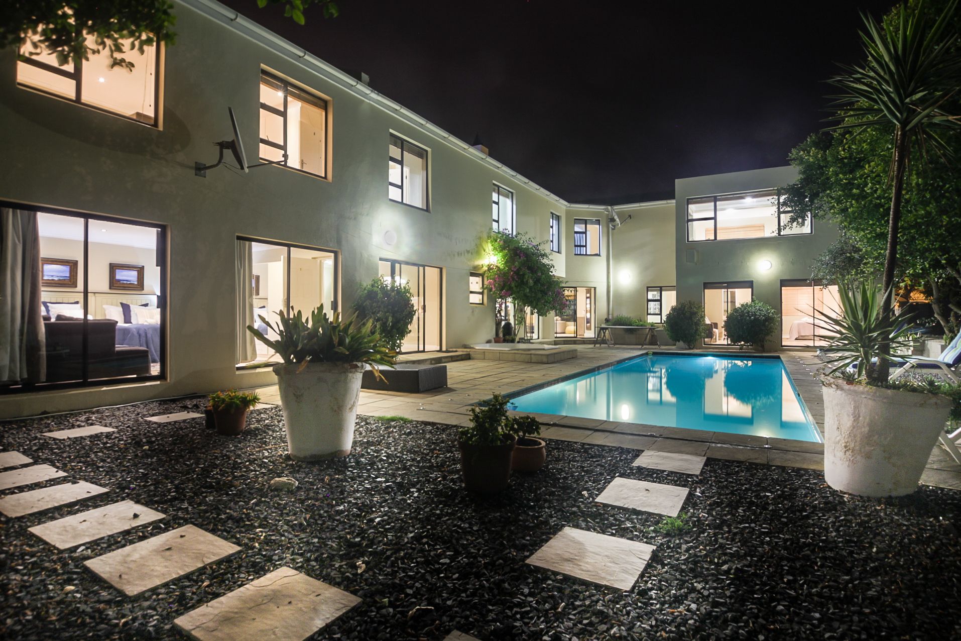 A modern hotel with a swimming pool, potted plants, and a well-lit outdoor area.
