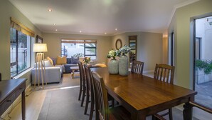 A spacious dining area with a wooden table and chairs, a sofa, and a lamp. - Atlantic Bay Lodge (Cape Town)