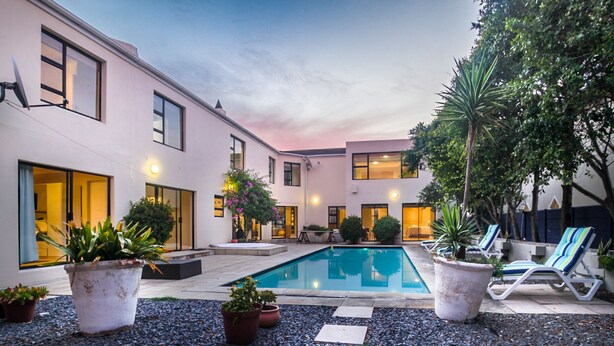 A modern outdoor pool area with a clear blue pool, surrounded by potted plants and lounge chairs. - Atlantic Bay Lodge (Cape Town)