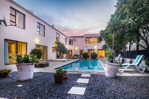 A modern outdoor pool area with a clear blue pool, surrounded by potted plants and lounge chairs. - Atlantic Bay Lodge (Cape Town)