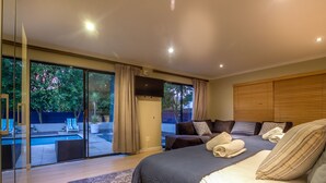 A modern bedroom with a large bed, a glass door leading to a pool area, and a view of trees. - Atlantic Bay Lodge (Cape Town)