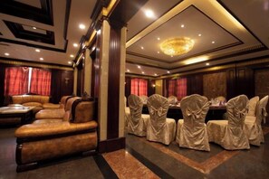 Habitación de hotel con zona de estar, una mesa de comedor y sillas cubiertas con manteles.