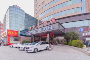 Un hotel con fachada moderna, una entrada destacada y un estacionamiento con varios coches.