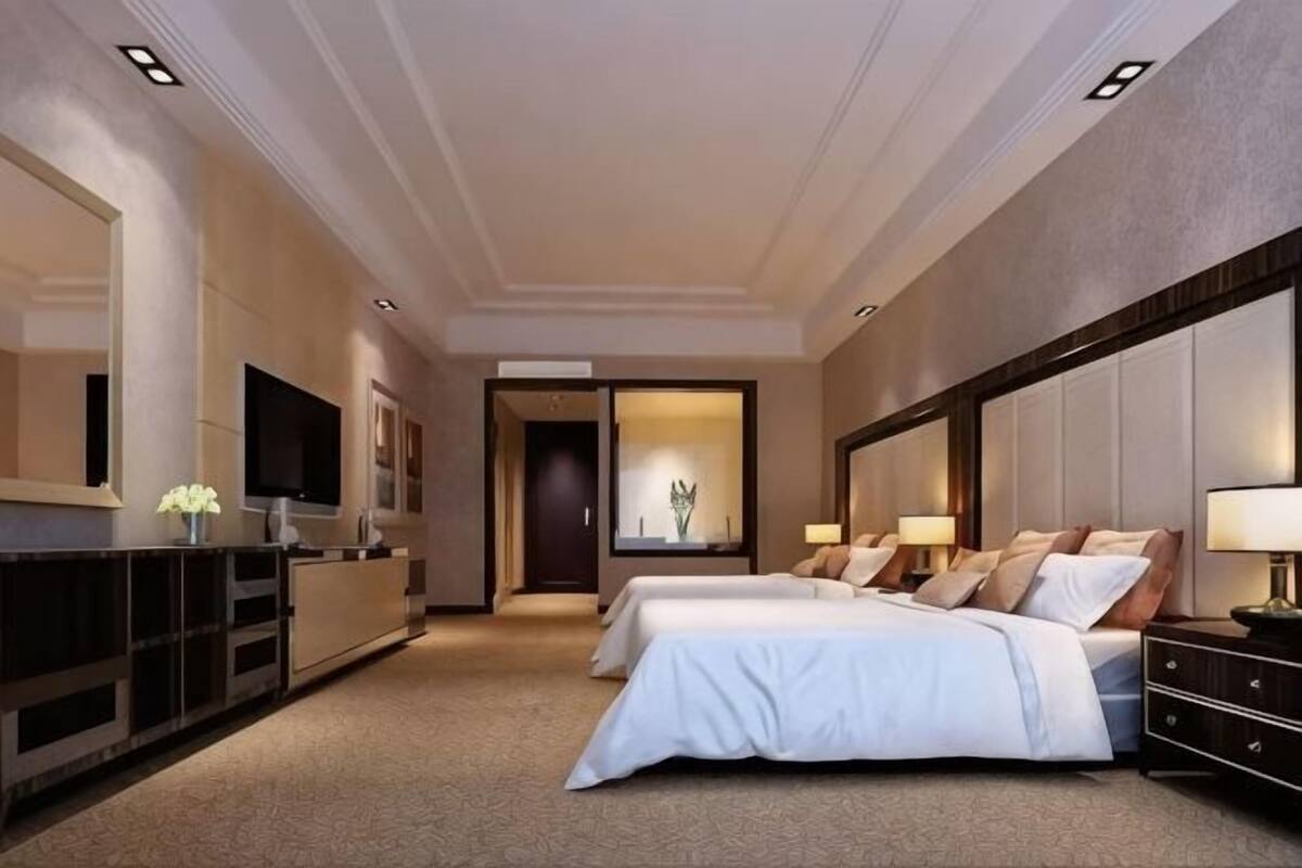 A hotel room with two beds, a TV, a desk, and a large mirror.