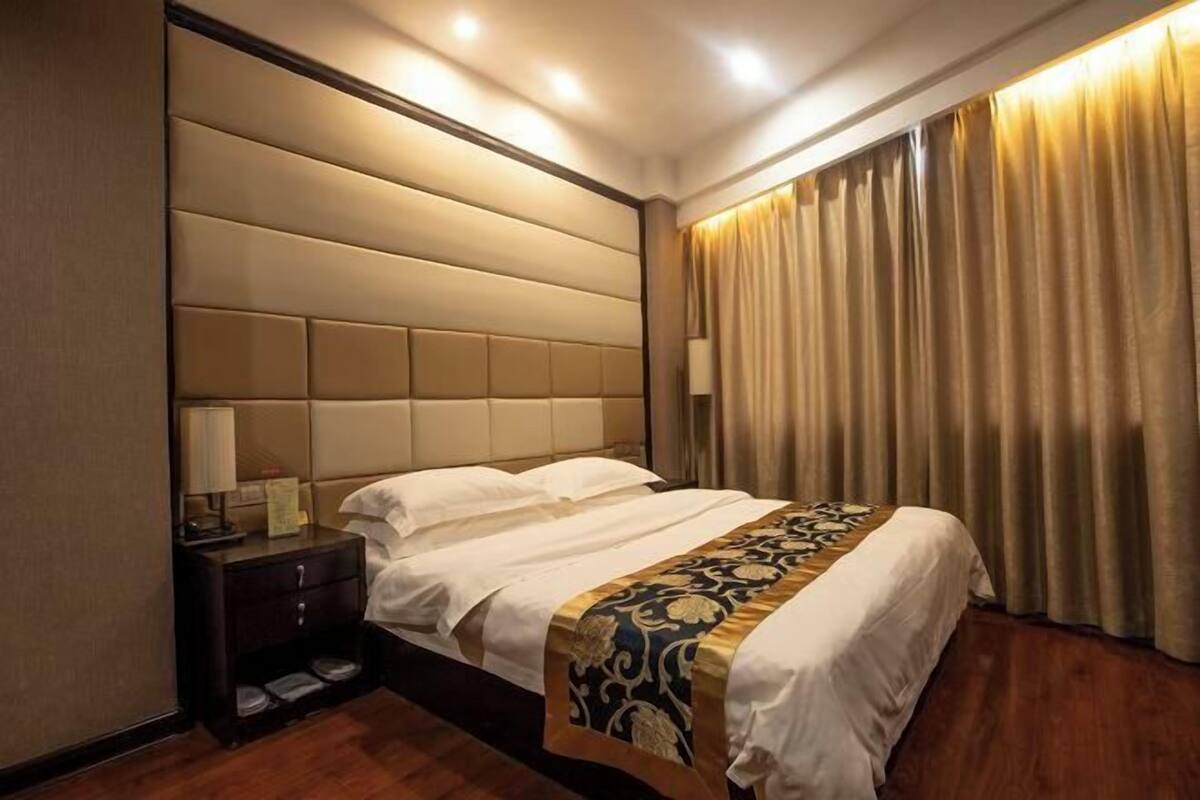 A hotel room with a large bed, a nightstand, and a window with curtains.