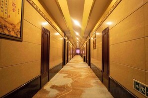 Pasillo de hotel con puertas a ambos lados, alfombra estampada y un letrero que indica la dirección al ascensor.