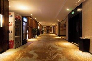 A hotel corridor with a carpeted floor, vending machines, and a reception area. - Xiangyu Hotel (Shangqiu Municipal Government High-speed Railway Station) (Shangqiu)