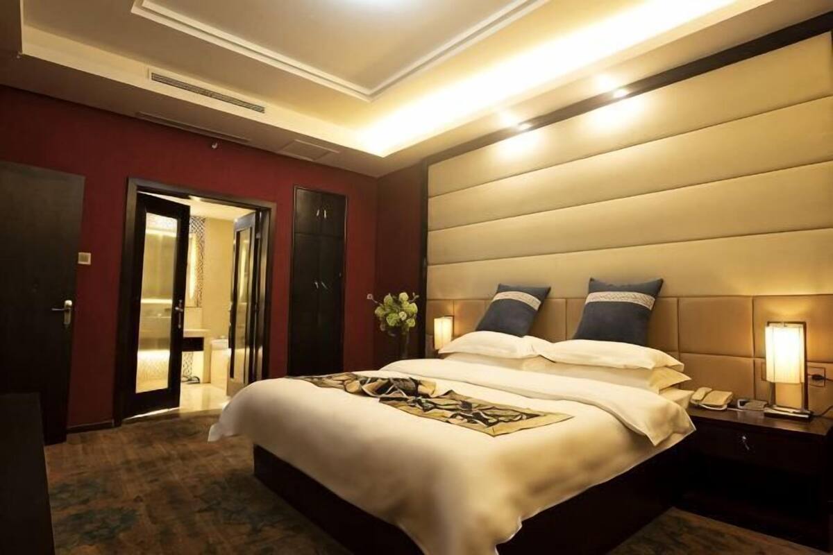 A hotel room with a large bed, a nightstand with a lamp, and a door leading to a bathroom.