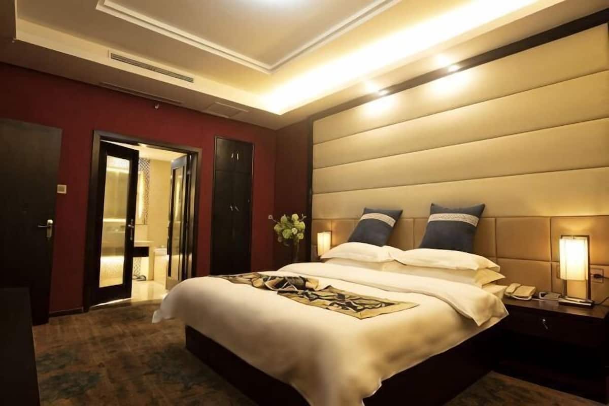 Una habitación de hotel con una cama grande, una mesita de noche con una lámpara y una puerta que da al baño.