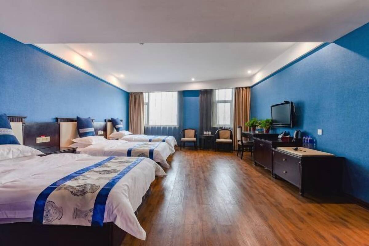 A hotel room with three beds, a desk, a television, and a window.