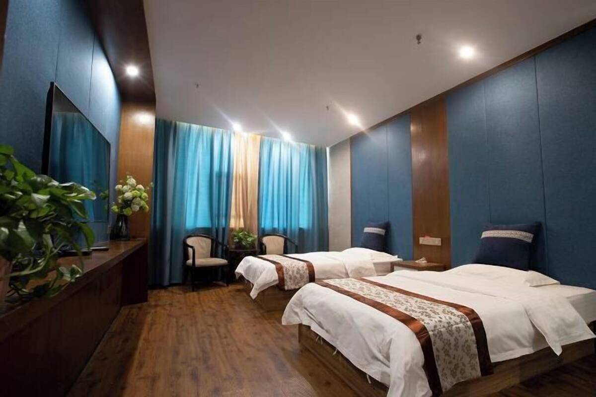 A hotel room with two beds, a desk, a chair, and a TV.