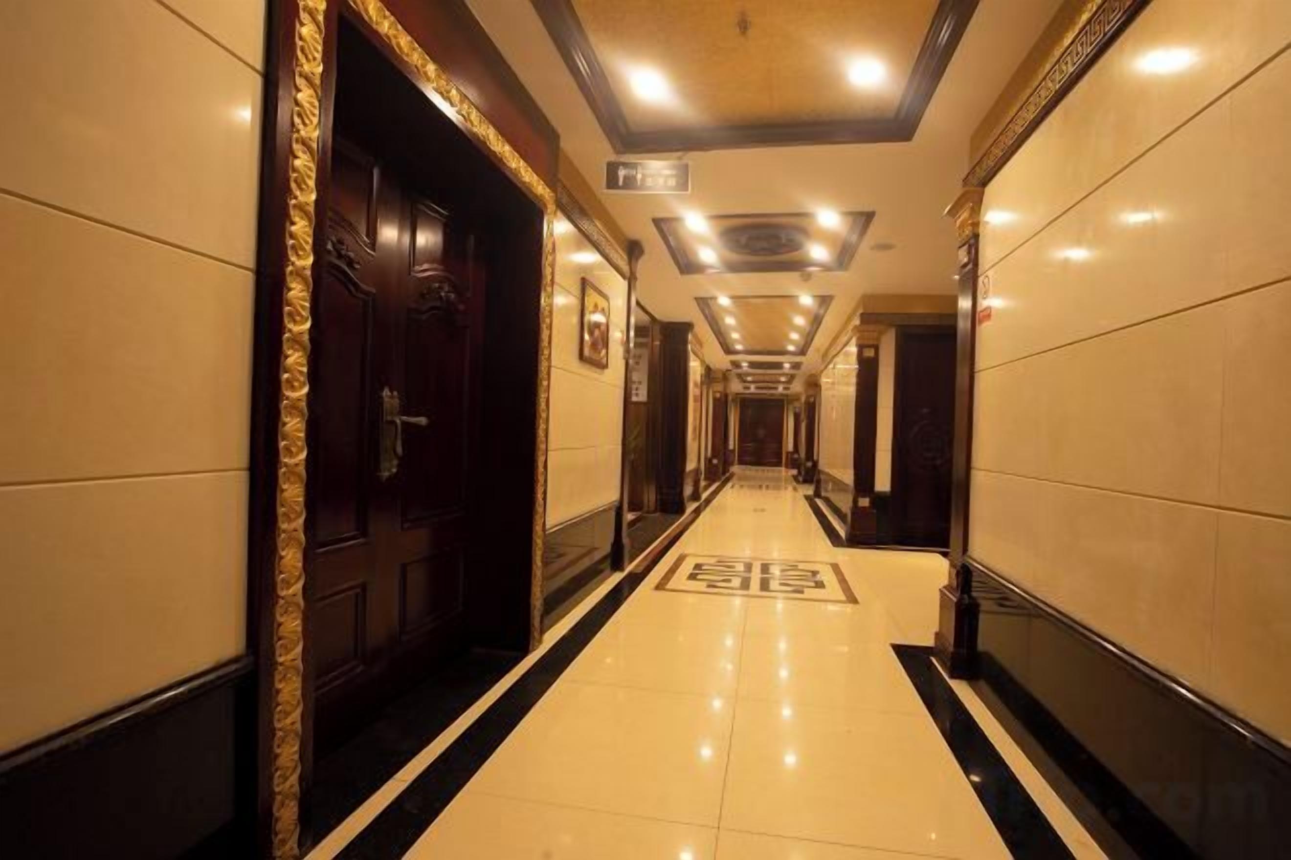 A hotel hallway with a polished floor, a door with a decorative frame, and a sign indicating the direction to the lobby.