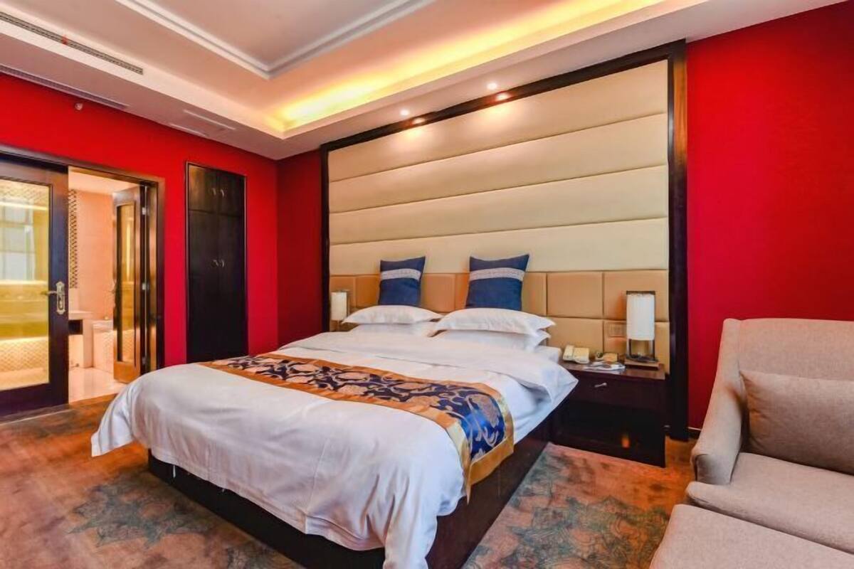 A hotel room with a large bed, a nightstand, a chair, and a red wall.