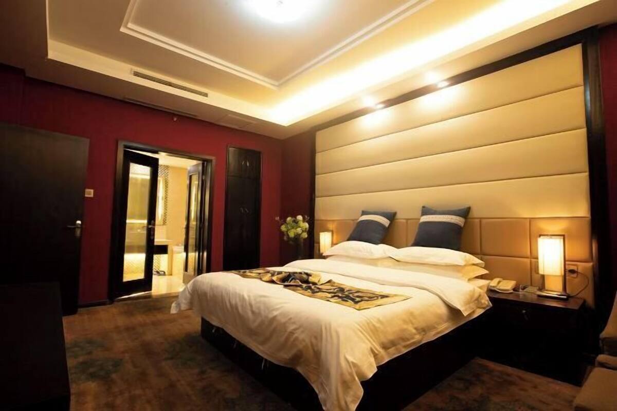 A hotel room with a large bed, bedside lamps, a nightstand, and a door leading to another room.