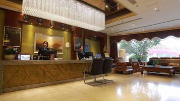 A hotel reception area with a marble counter, two receptionists, a seating area with sofas, and a large window with a view.
