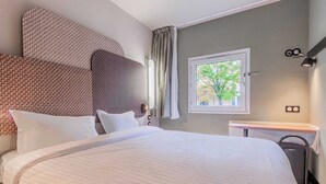 Une chambre d’hôtel avec un grand lit, une table de chevet, une fenêtre donnant sur des arbres et un luminaire fixé au mur.