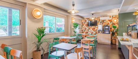A restaurant with multiple tables and chairs, a counter with a cash register, and a television mounted on the wall.