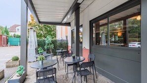 Un espace extérieur aménagé en terrasse, avec des tables et des chaises, entouré d’un petit muret et doté d’une partie couverte.