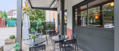 An outdoor patio area with tables and chairs, surrounded by a low wall and a covered section.