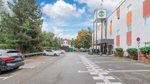 Un parking rempli de voitures, un bâtiment sur lequel on peut lire l’inscription « B&B HOTELS », et un passage piéton.