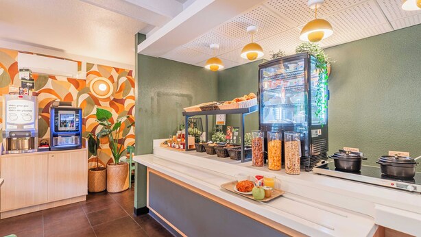 Un espace d’accueil d’hôtel comprenant une machine à café, un distributeur de boissons en libre-service et un buffet proposant divers plats.