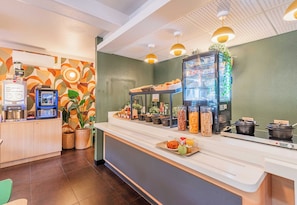 A hotel reception area with a coffee machine, a self-service beverage station, and a buffet counter with various food items.