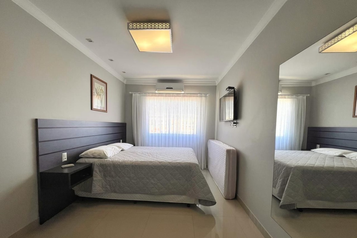 A modern hotel room with a large bed, a bedside table, a mirror, and a ceiling light.