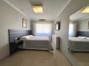 A modern hotel room with a large bed, a bedside table, a mirror, and a ceiling light.