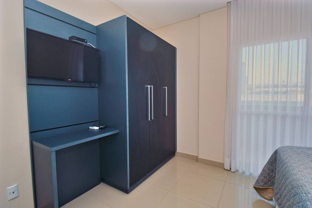 Une chambre avec une armoire bleu foncé, un téléviseur à écran plat fixé au mur et un lit recouvert d’une couvre-lit à motifs.