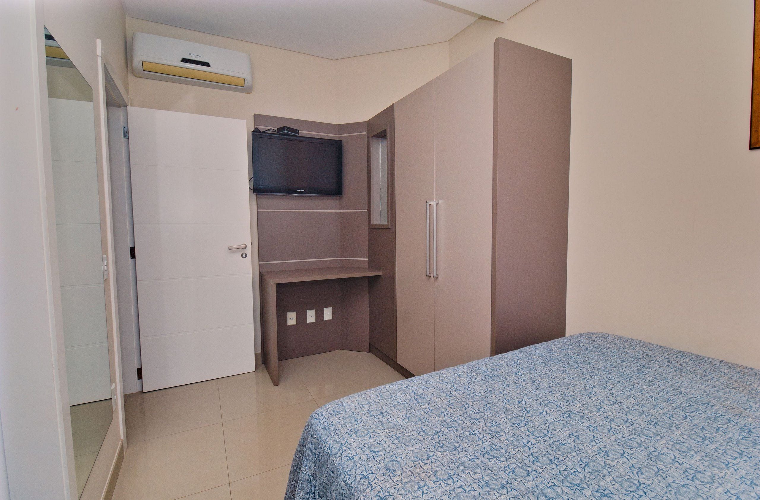 A bedroom with a bed, a wardrobe, a TV, and an air conditioning unit.