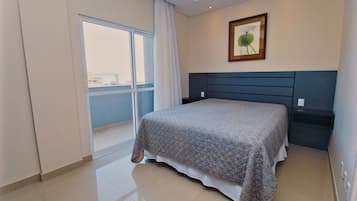 A modern bedroom with a large bed, a nightstand, a framed picture on the wall, and a sliding glass door leading to a balcony.