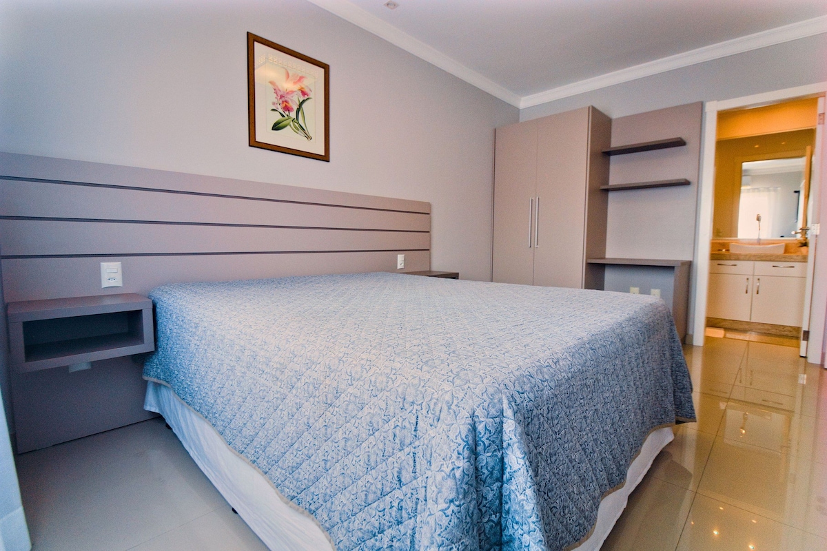 A bedroom with a bed, a nightstand, a wardrobe, and a bathroom visible through an open door.