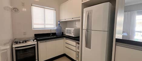 Una cocina con gabinetes blancos, estufa, refrigerador y microondas.