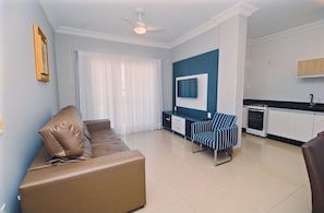 Una sala de estar moderna con un sofá, un televisor montado en la pared, una zona de comedor y una cocina.