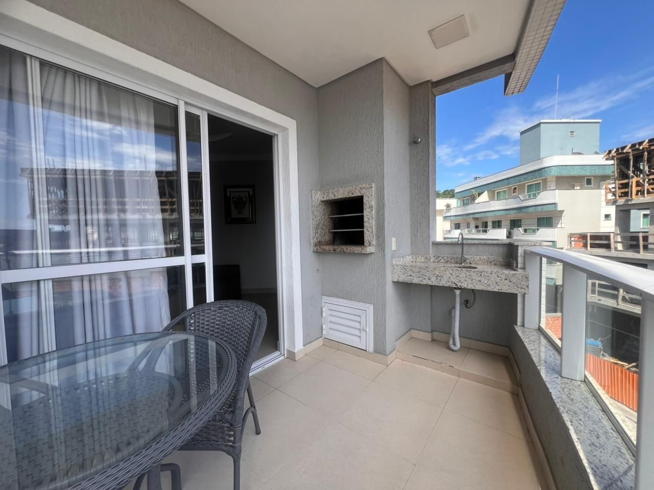 A balcony with a glass table and chairs, a built-in sink, and a view of neighboring buildings.