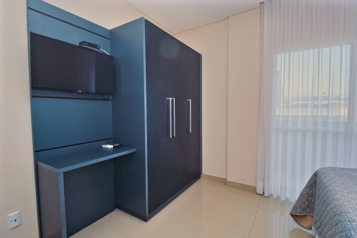 A bedroom with a dark blue wardrobe, a flat-screen TV mounted on the wall, and a bed with a patterned bedspread.