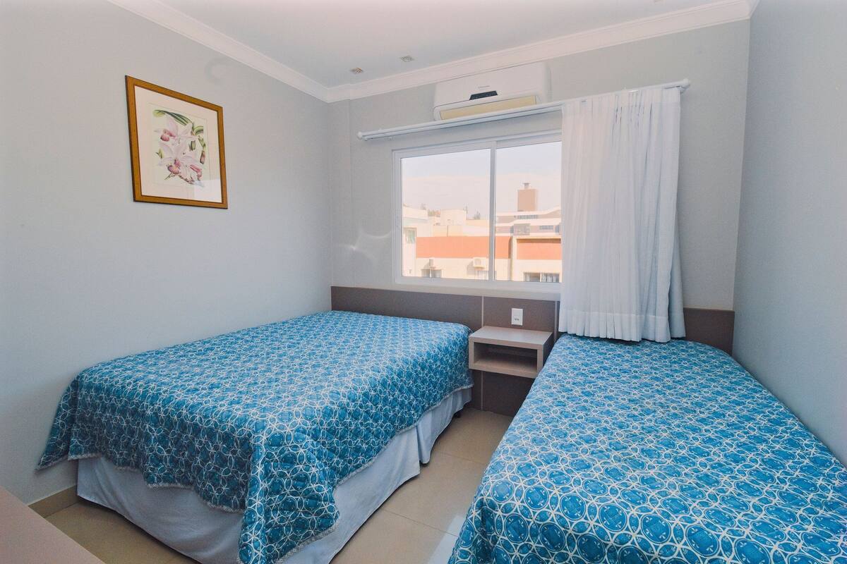 Une chambre avec deux lits, une fenêtre avec des rideaux, un bureau et un tableau encadré au mur.