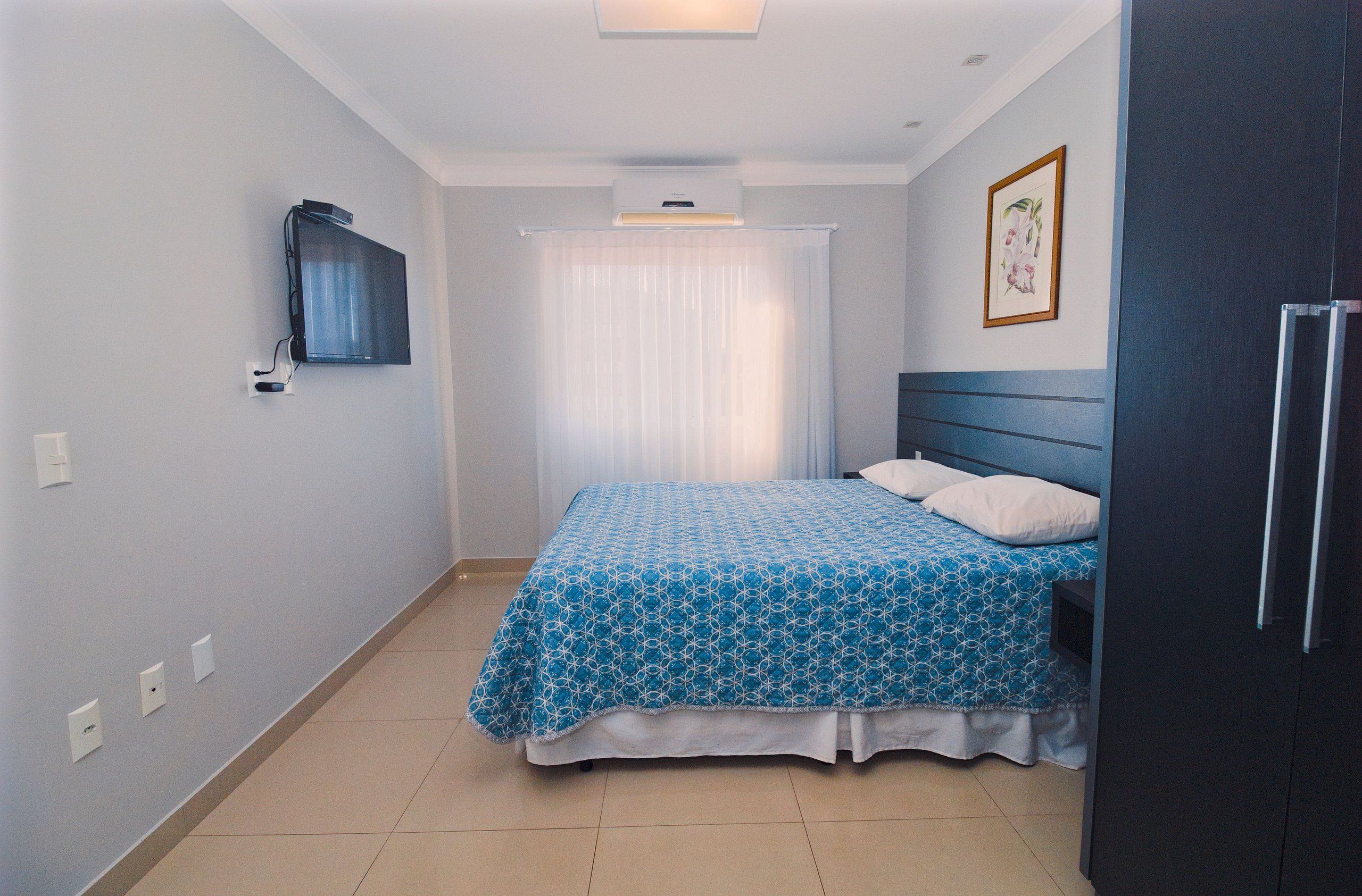 A bedroom with a bed, a TV mounted on the wall, a ceiling fan, and a framed picture on the wall.