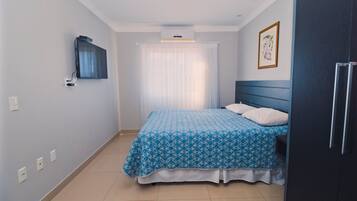 A bedroom with a bed, a TV mounted on the wall, a ceiling fan, and a framed picture on the wall.