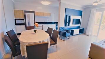 A modern kitchen with a dining area, a TV mounted on the wall, and a large window.