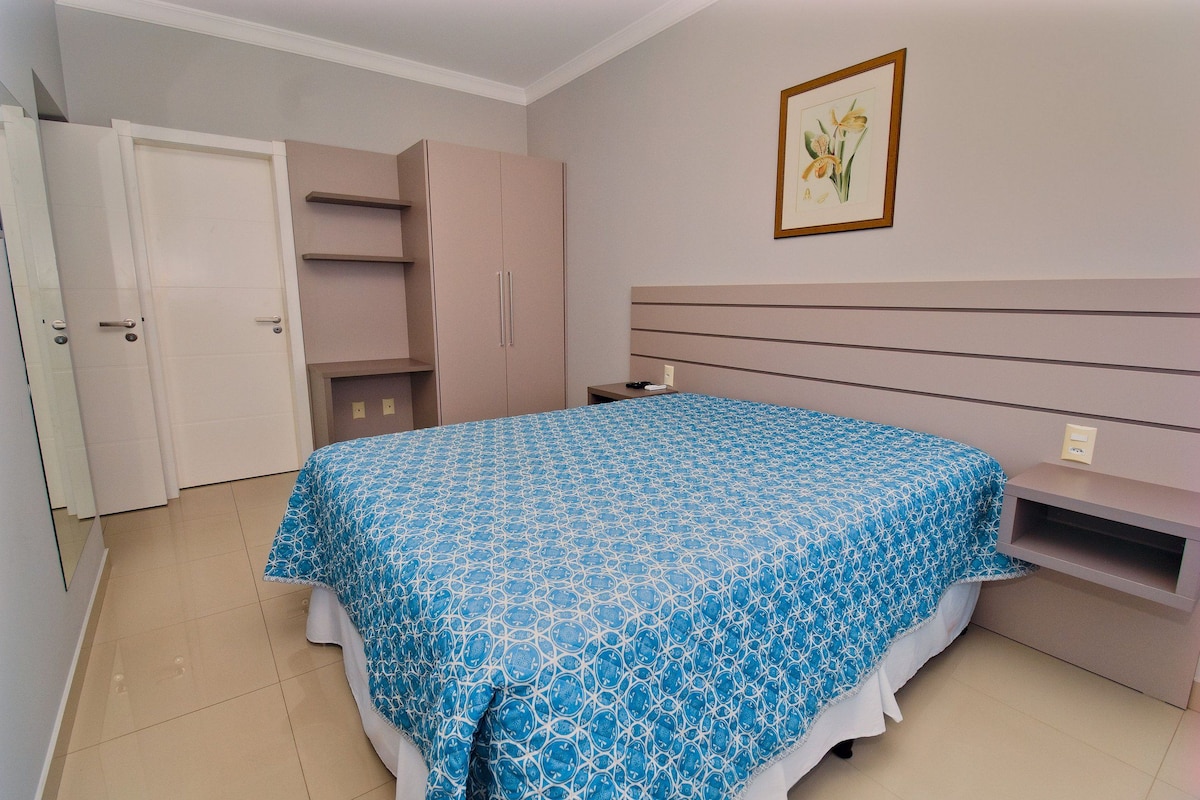 A bedroom with a bed, a wardrobe, a nightstand, and a framed picture on the wall.